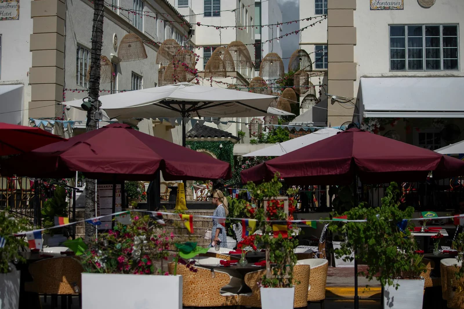 Ocean Drive’da açık hava restoran terası: bordo şemsiyeler, çiçekli saksılar ve kaldırıma dizilmiş masalar.